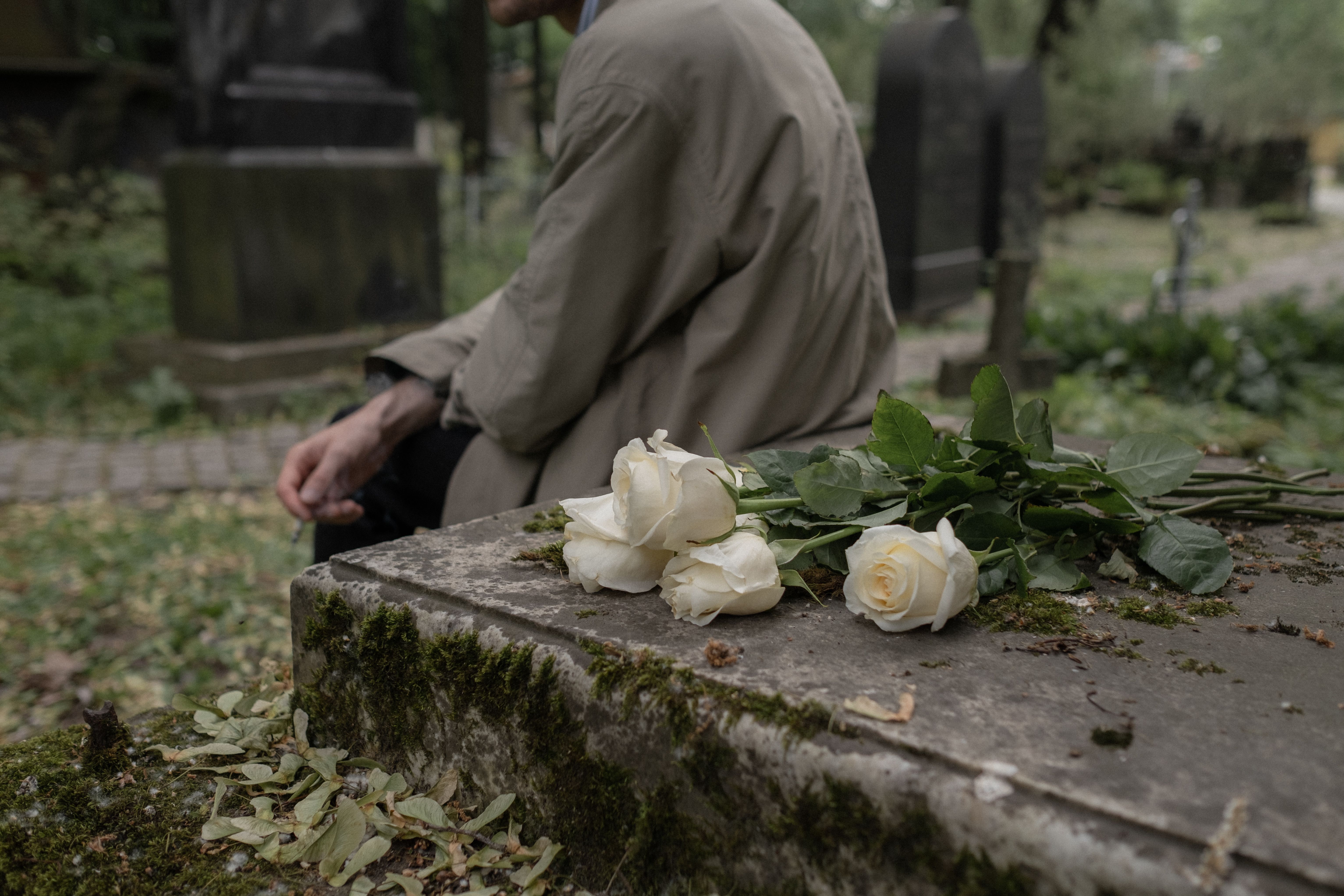 White roses on an old stone grave, with a person sitting beside it