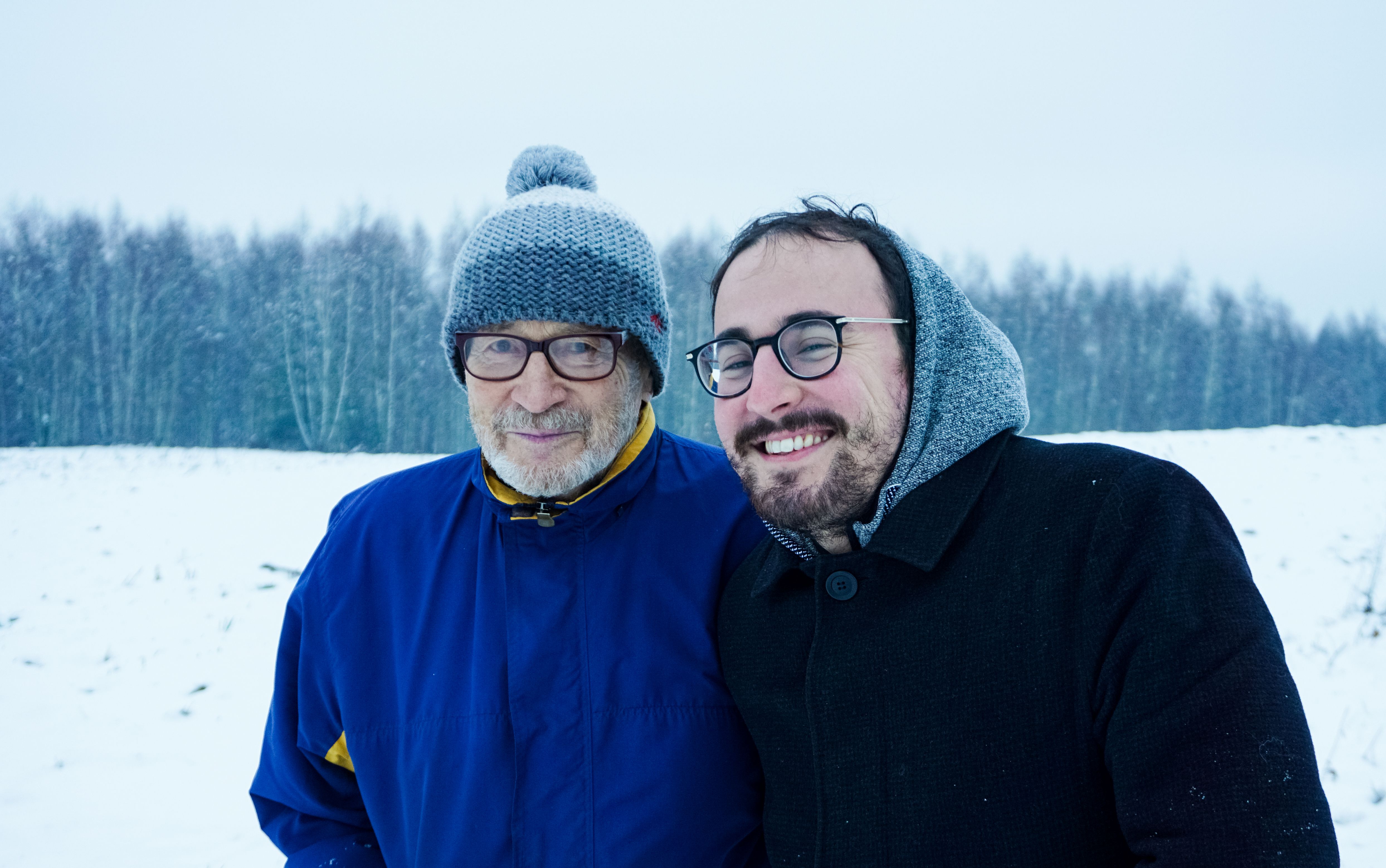 An older man and his grandson smiling together in the snow