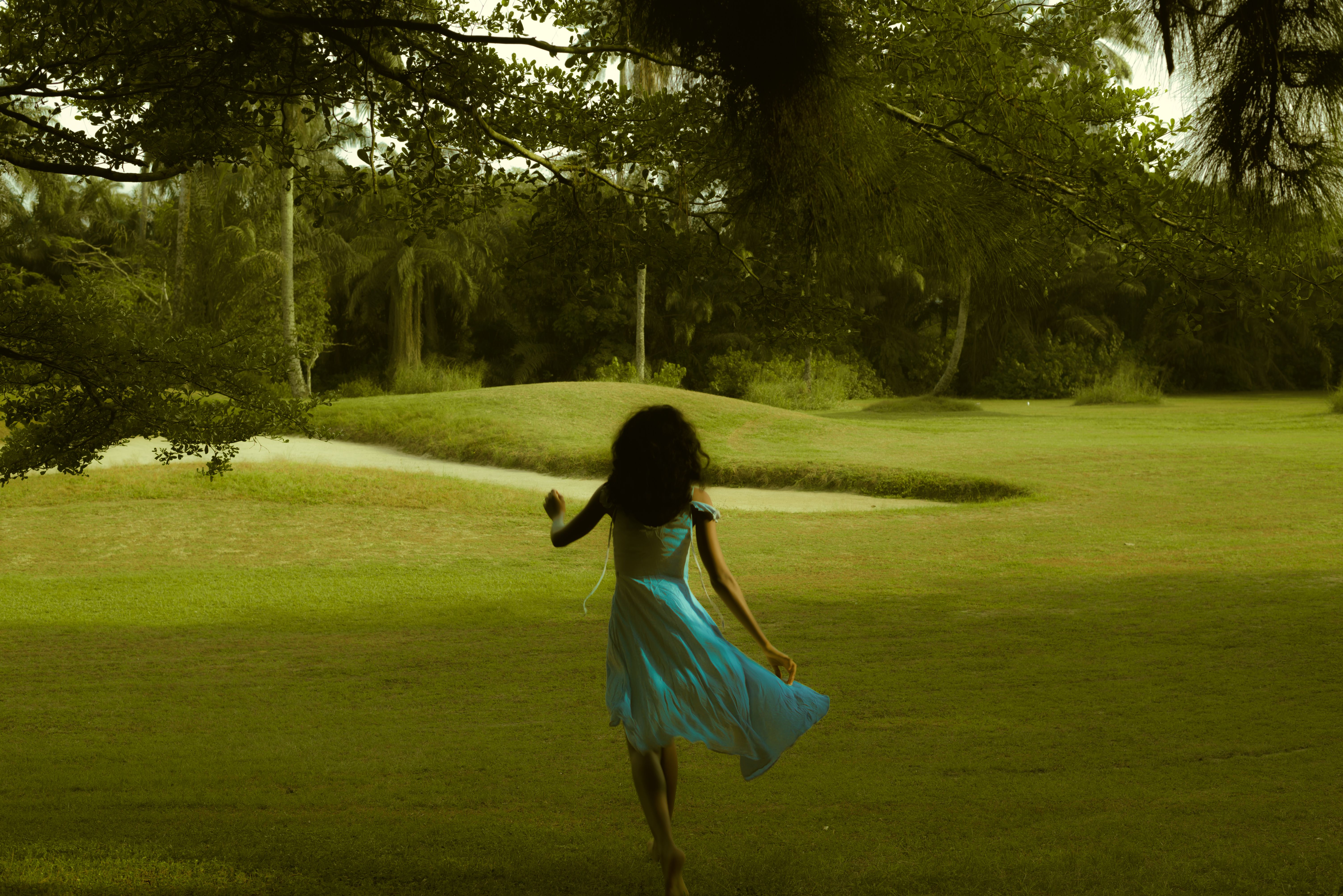 A girl in a blue dress walking across a lawn