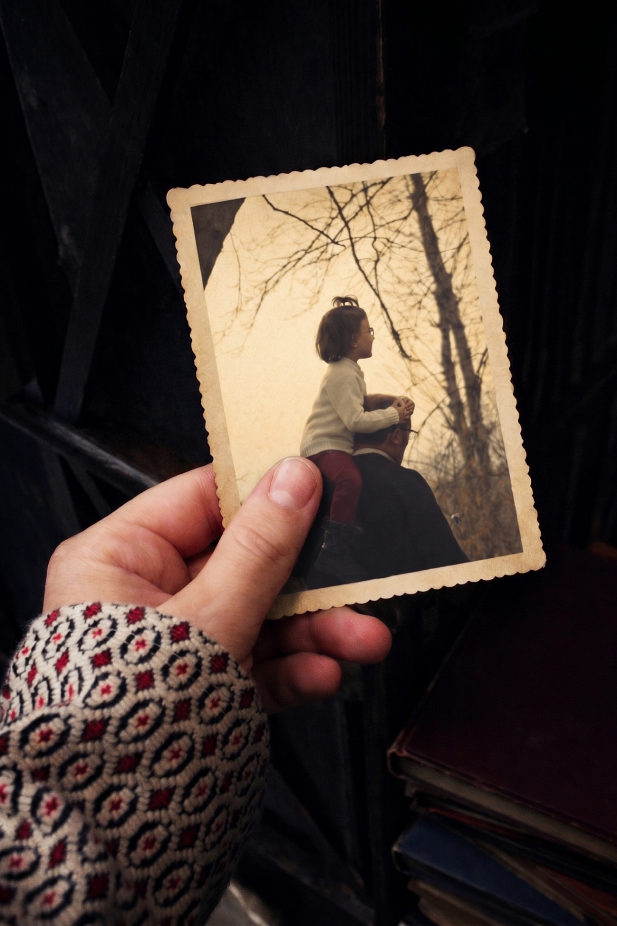 A hand holding a vintage photograph of a father with a child on his shoulders
